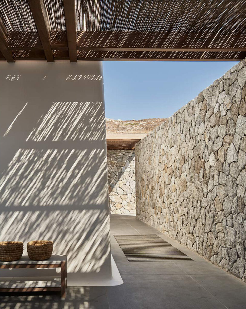 The design of Villa Mandra, a summer home in Mykonos, Greece, uses traditional elements of lime wash, stone, and wood to blend with its environment.