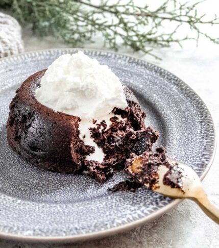 A speckled grey ceramic plate with a molten hot chocolate cake oozing gooey chocolate topped with whipped cream.