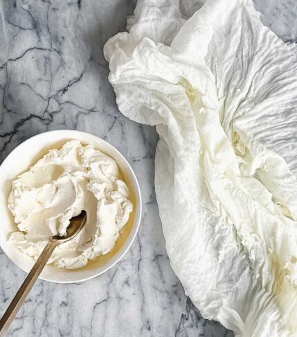 A bowl of homemade labneh yogurt cheese next to a cheesecloth used to strain the cheese.