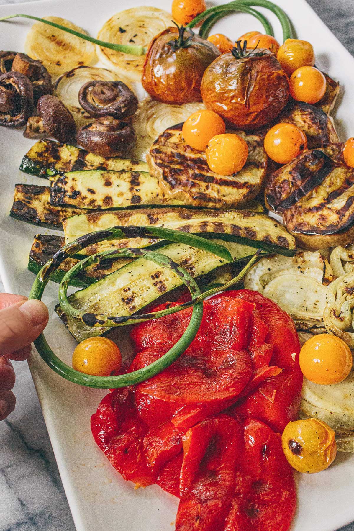 A platter of grilled summer vegetables: zucchini, red peppers, onions, mushrooms, eggplant, tomatoes, garlic scapes