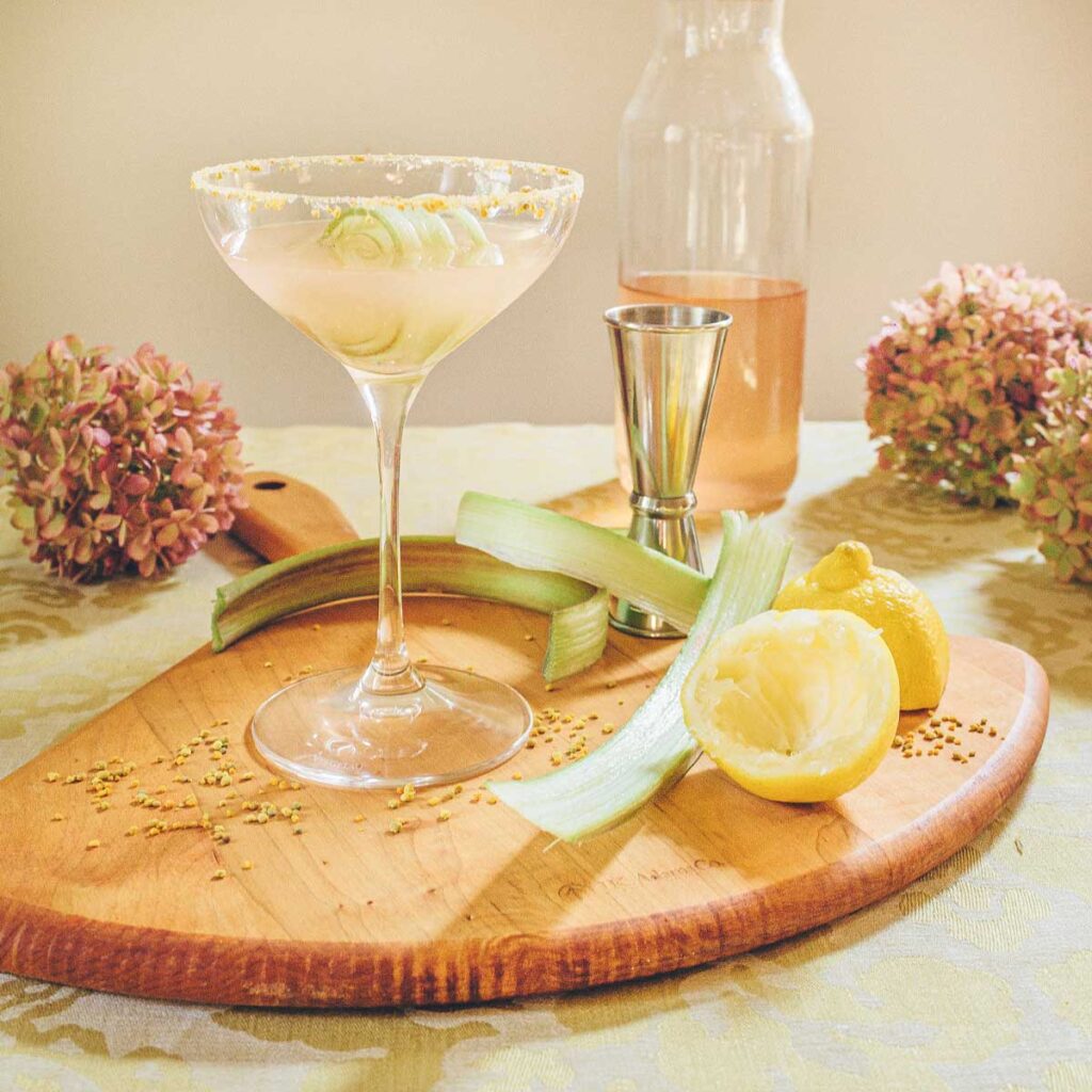 A cutting board with a coupé glass filled with a Rhubarb Bee's Knees cocktail.