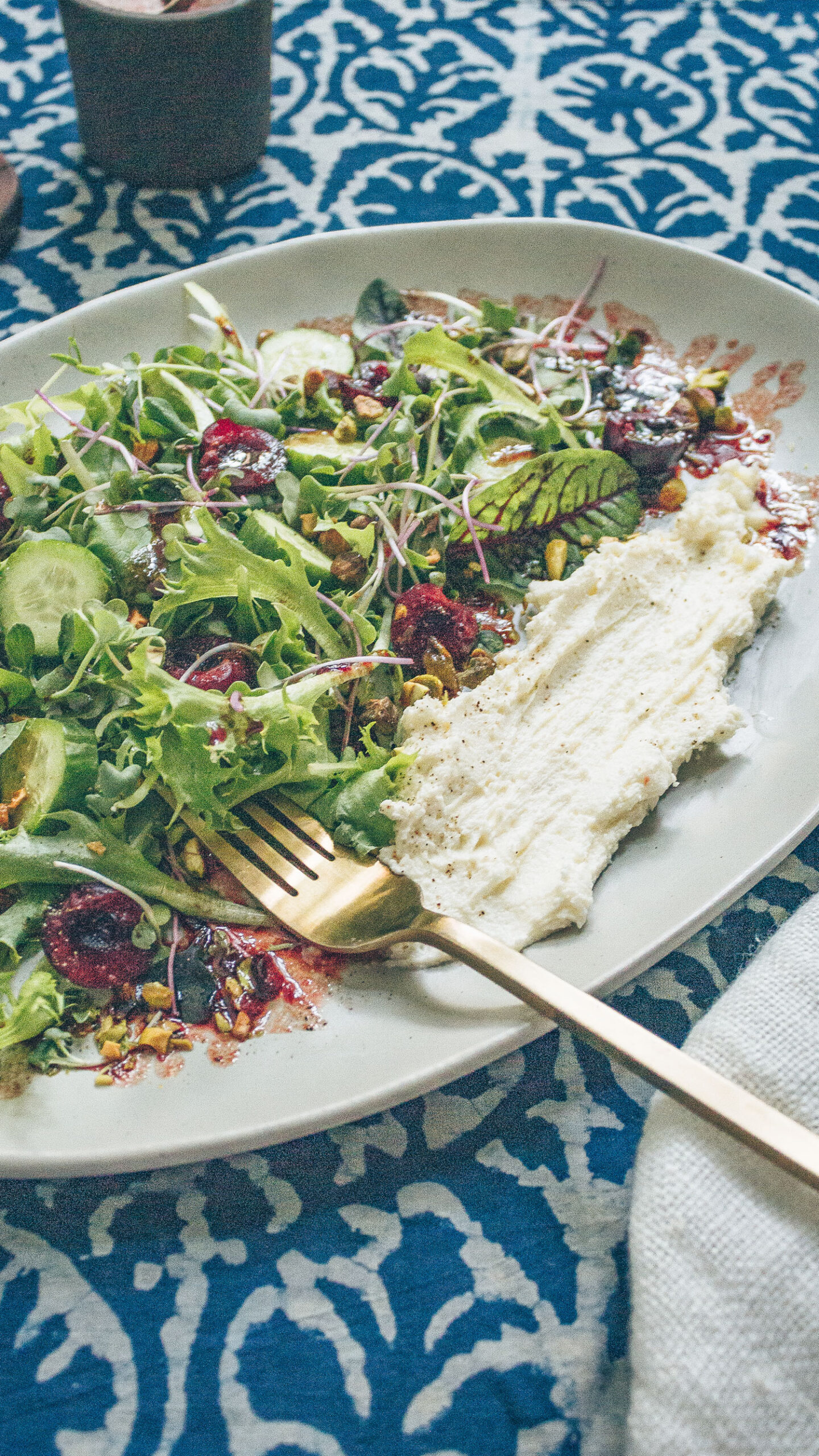 Mixed arugula salad on a plate with fresh cherries, pistachios, and whipped feta.