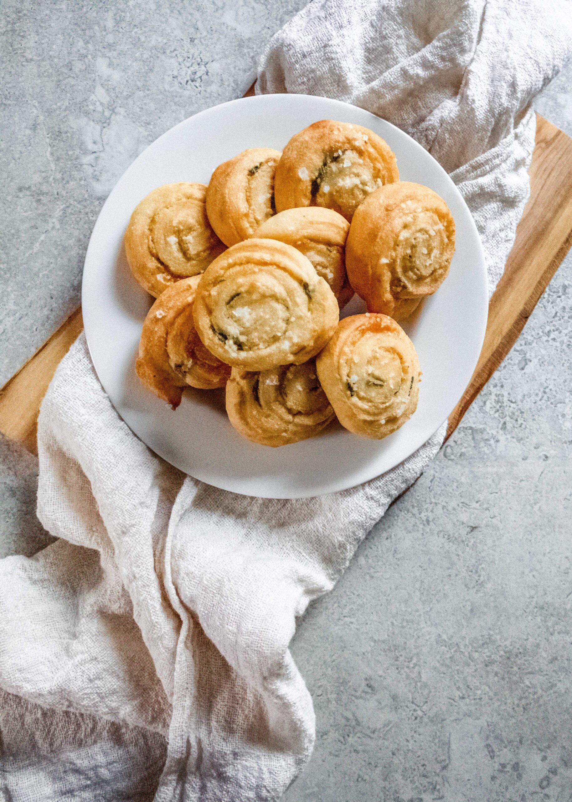 A plate of Parmesan Sage Pinwheels on top of a linen napkin and cutting board.