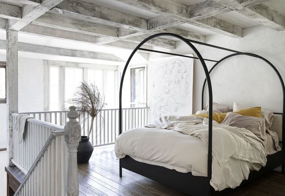 An open bedroom with a balcony under white plaster coated wood ceiling beams.