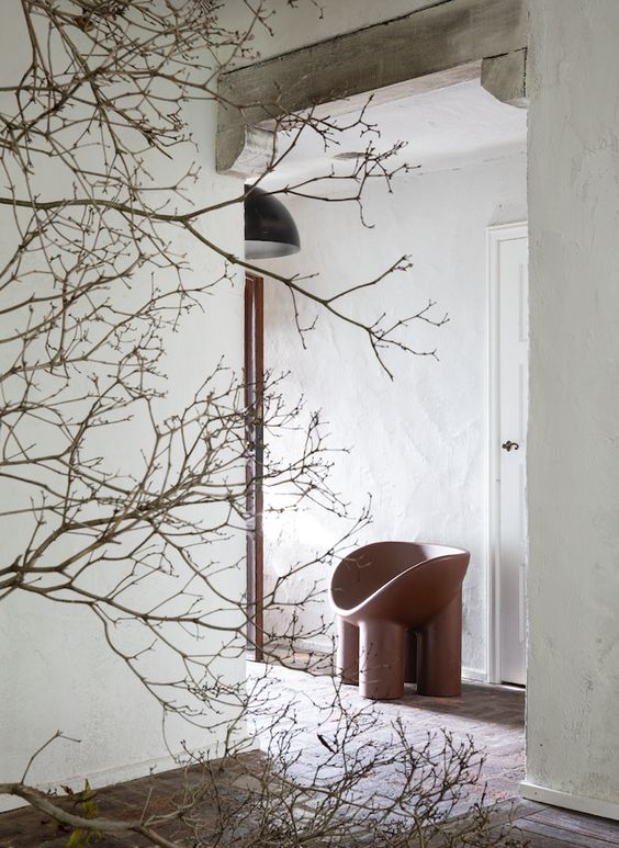 A white plaster walled hallway with a vase of tree branches and a modern wood stool.