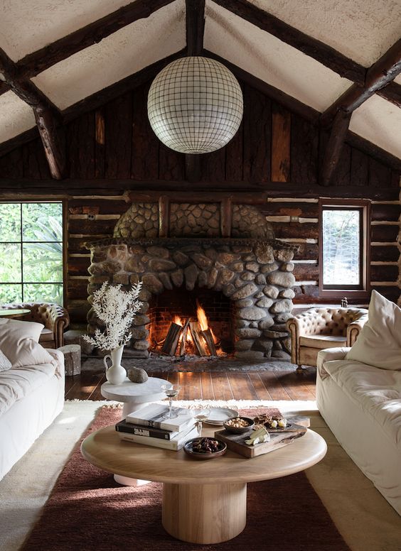 A modern rustic cottage living room with log beams and walls and a stone fireplace.