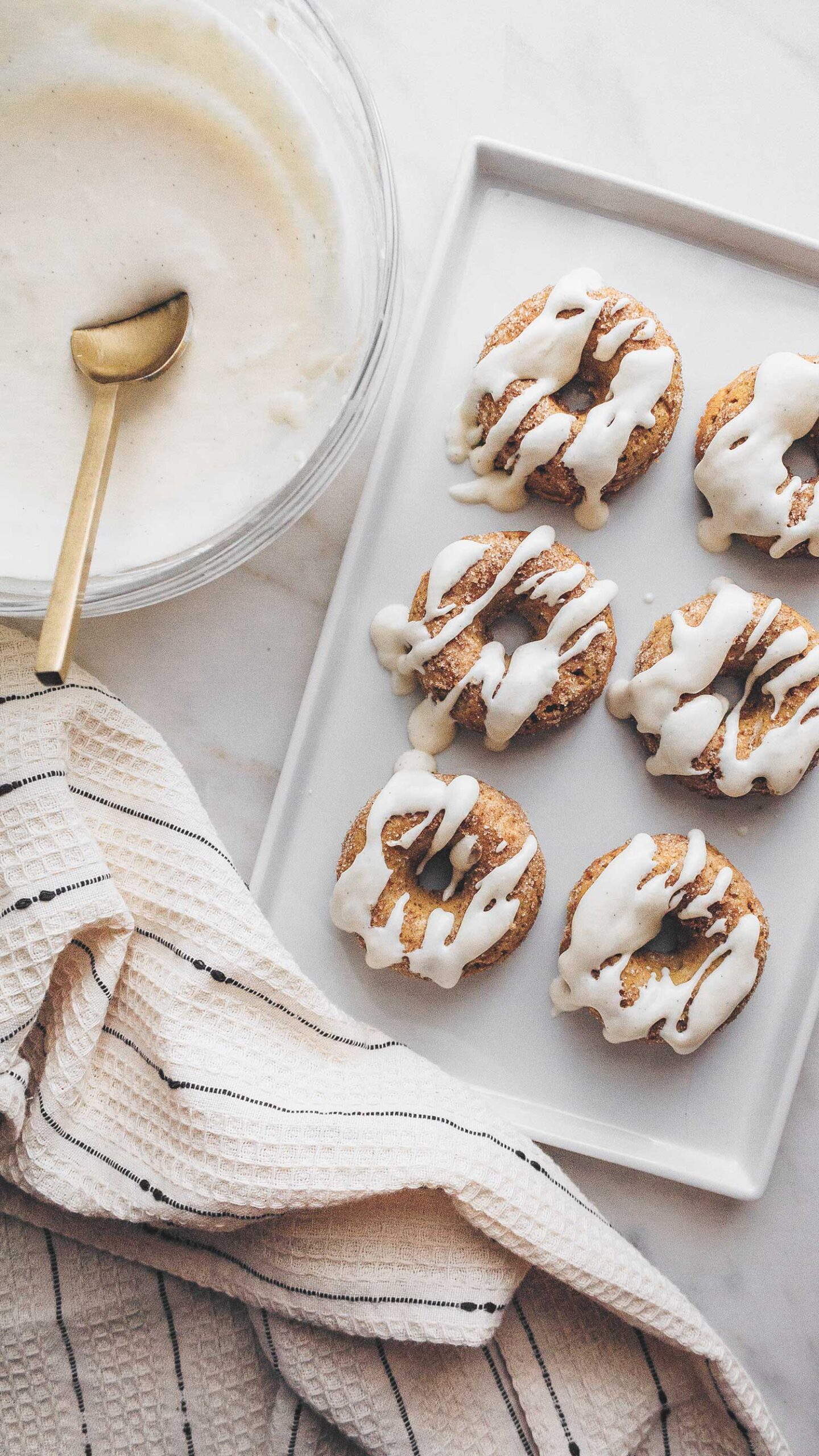 Keto pumpkin spice donuts drizzled with cream cheese glaze on a rectangular white platter.