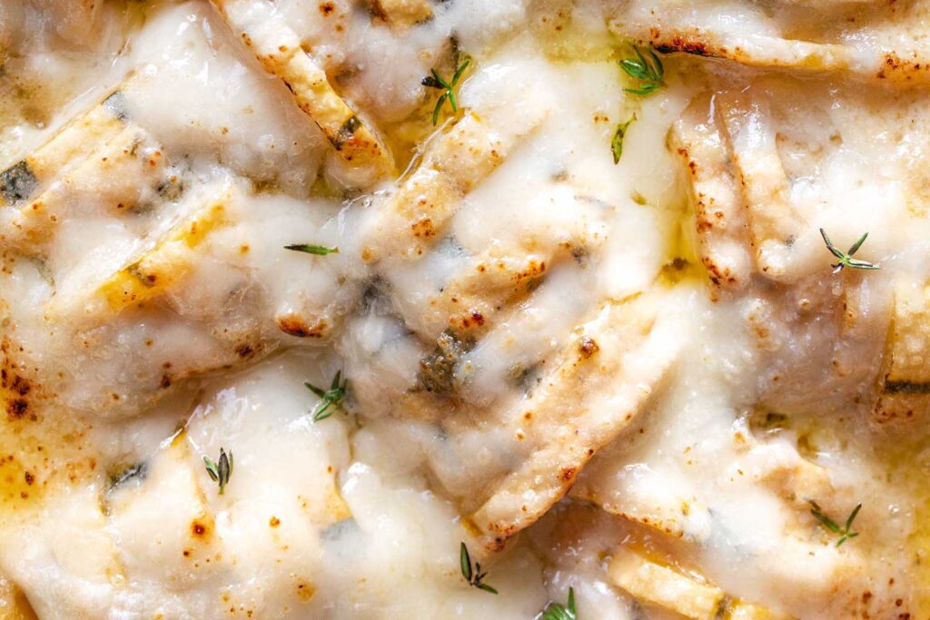 A closeup of Delicata Squash Gruyere Gratin covered in melted cheese and fresh thyme.