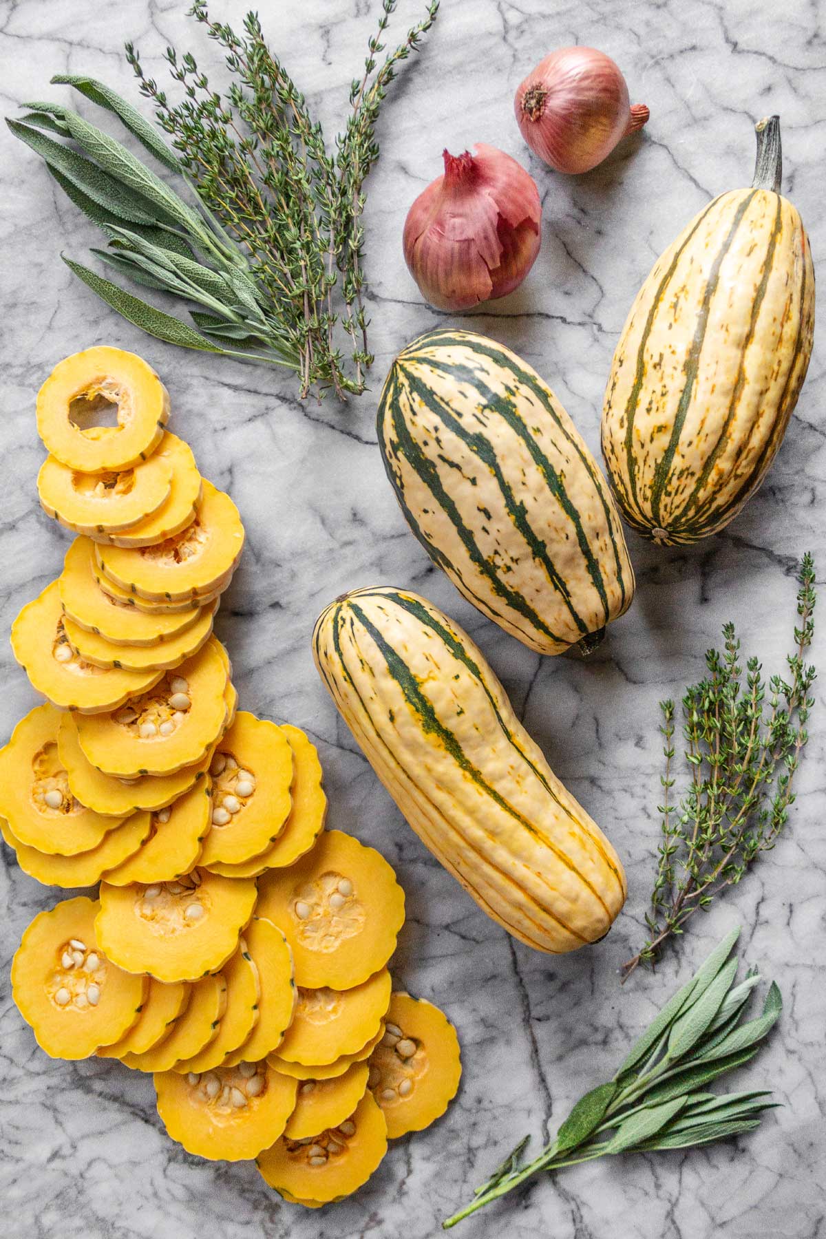 Some of the ingredients for Delicata Squash Gruyere Gratin, laid out on a marble slab: Delicata Squash, Shallots, Fresh Thymg & Sage