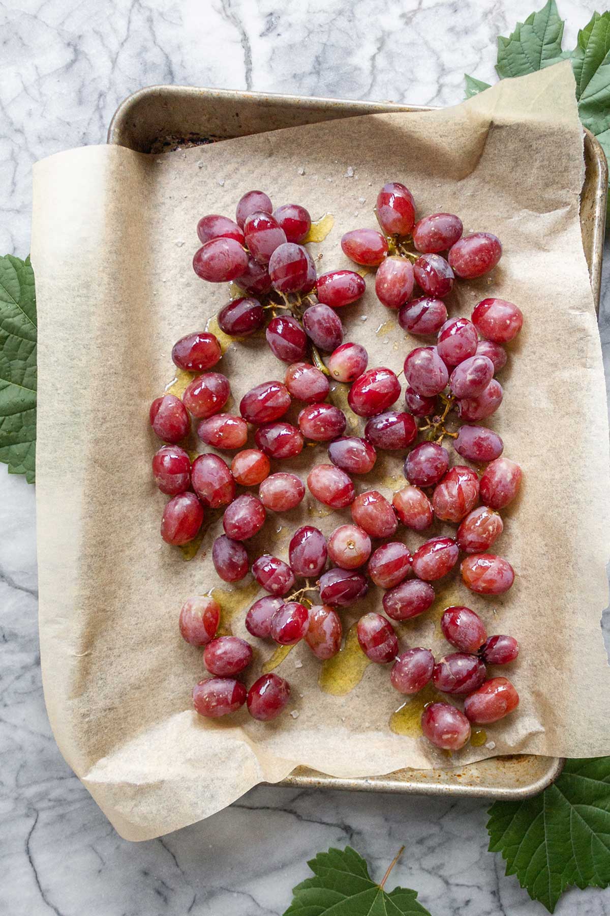 A parchment lined baking sheet layered with fresh red grapes drizzled in olive oil and sea salt.