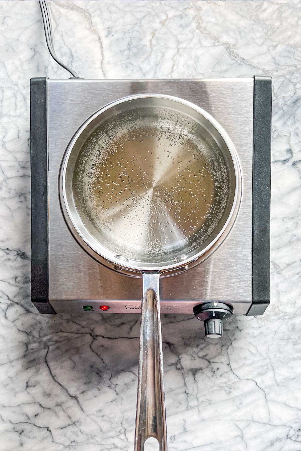 A pot of water starting to boil on a burner.