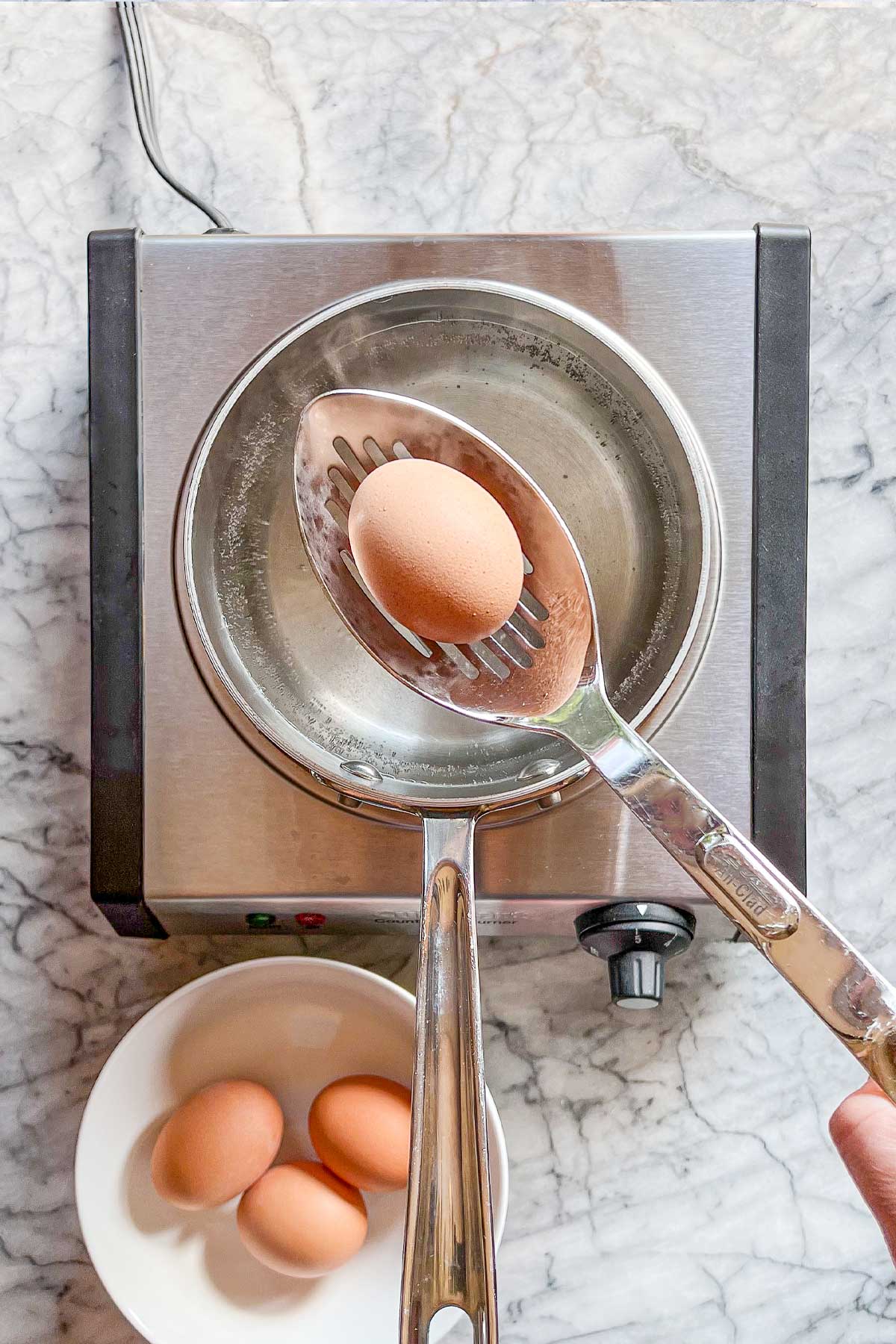 Large brown eggs being lowered into a pot of water on a stovetop burner.