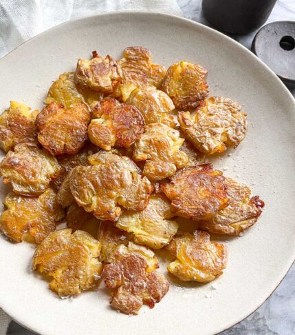 A plate filled with dark, crispy, roasted smashed potatoes sprinkled with sea salt.