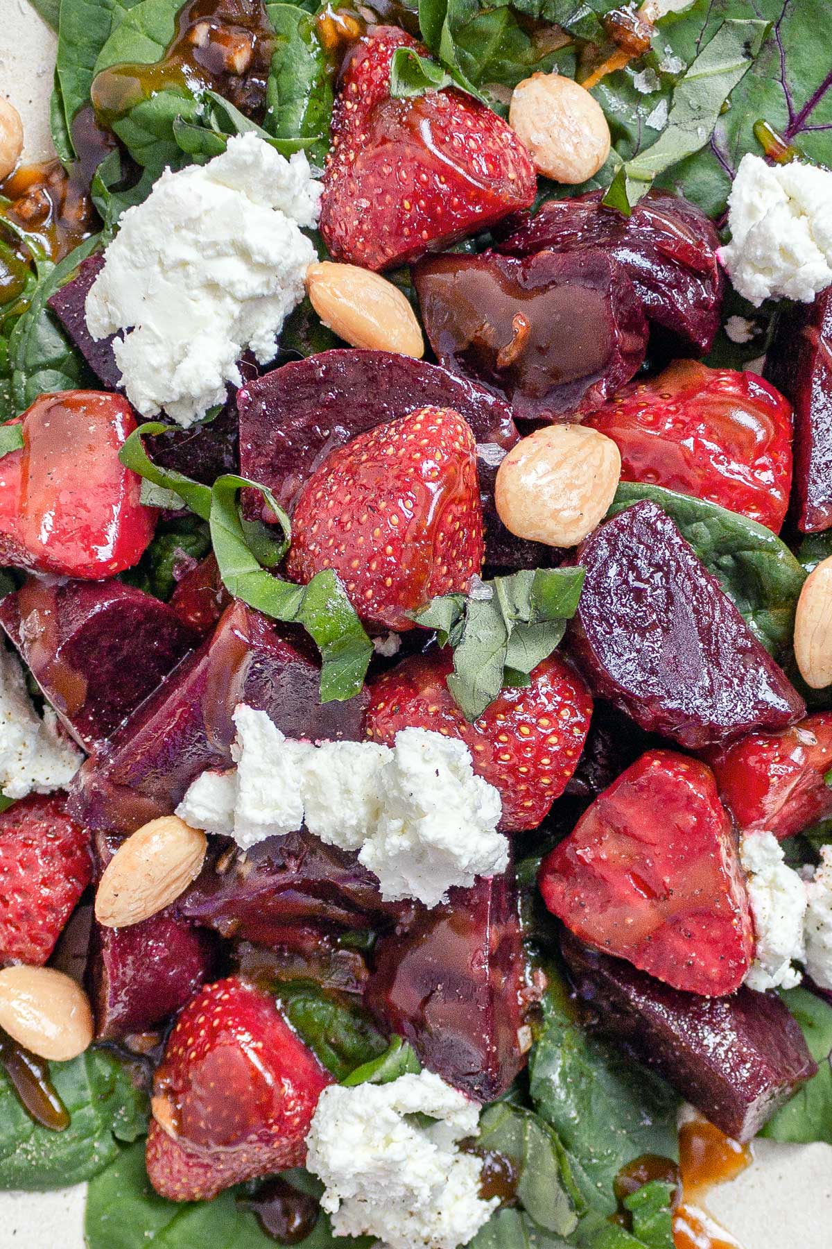A close up of a Summer Strawberry Salad with roasted beets, chunks of fresh goat cheese, Marcona almonds, and slivers of fresh basil, all tossed in a balsamic vinaigrette.