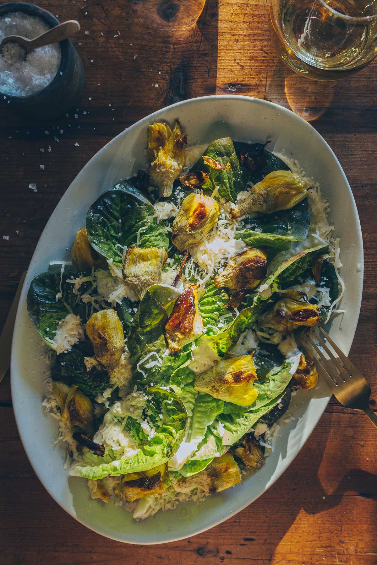 A serving platter with romaine lettuce leaves drizzled with an easy caesar dressing, artichoke hearts, garlic croutons, and parmesan cheese. 