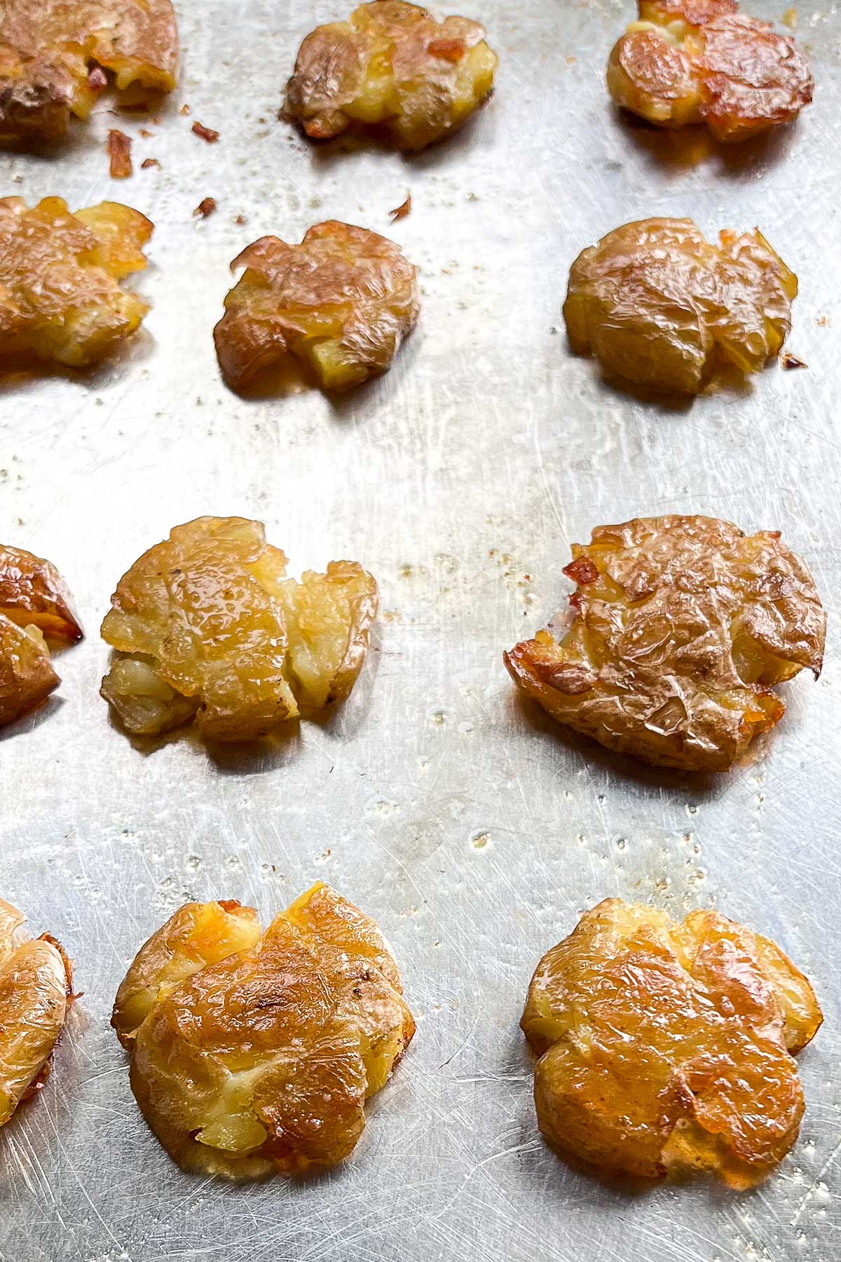 A baking sheet with roasted smashed potatoes evenly spaced, brown and crispy and glistening with olive oil and flakey sea salt.