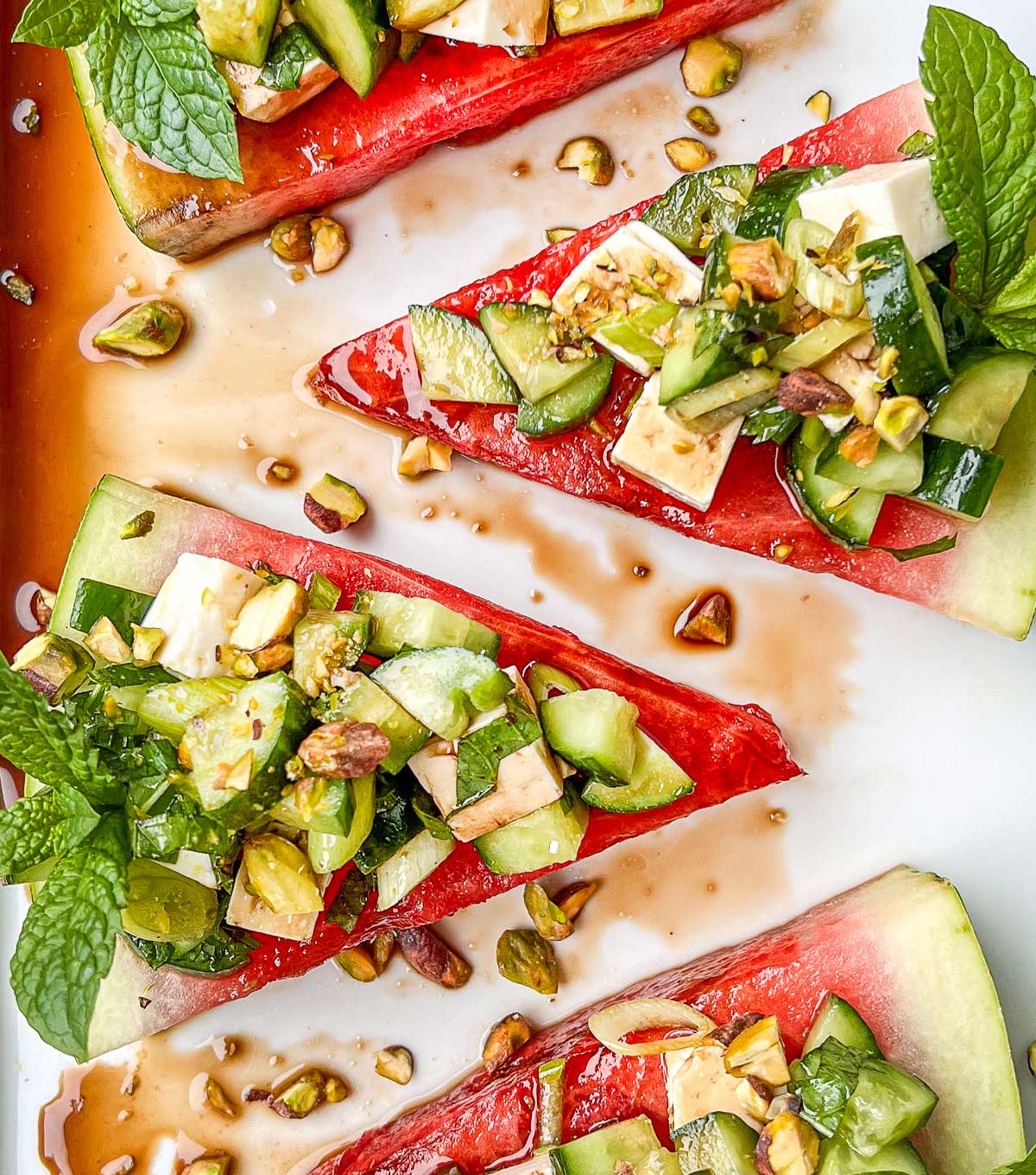 A close up of watermelon wedges topped with a watermelon cucumber mint salad topping and drizzled with balsamic vinegar.
