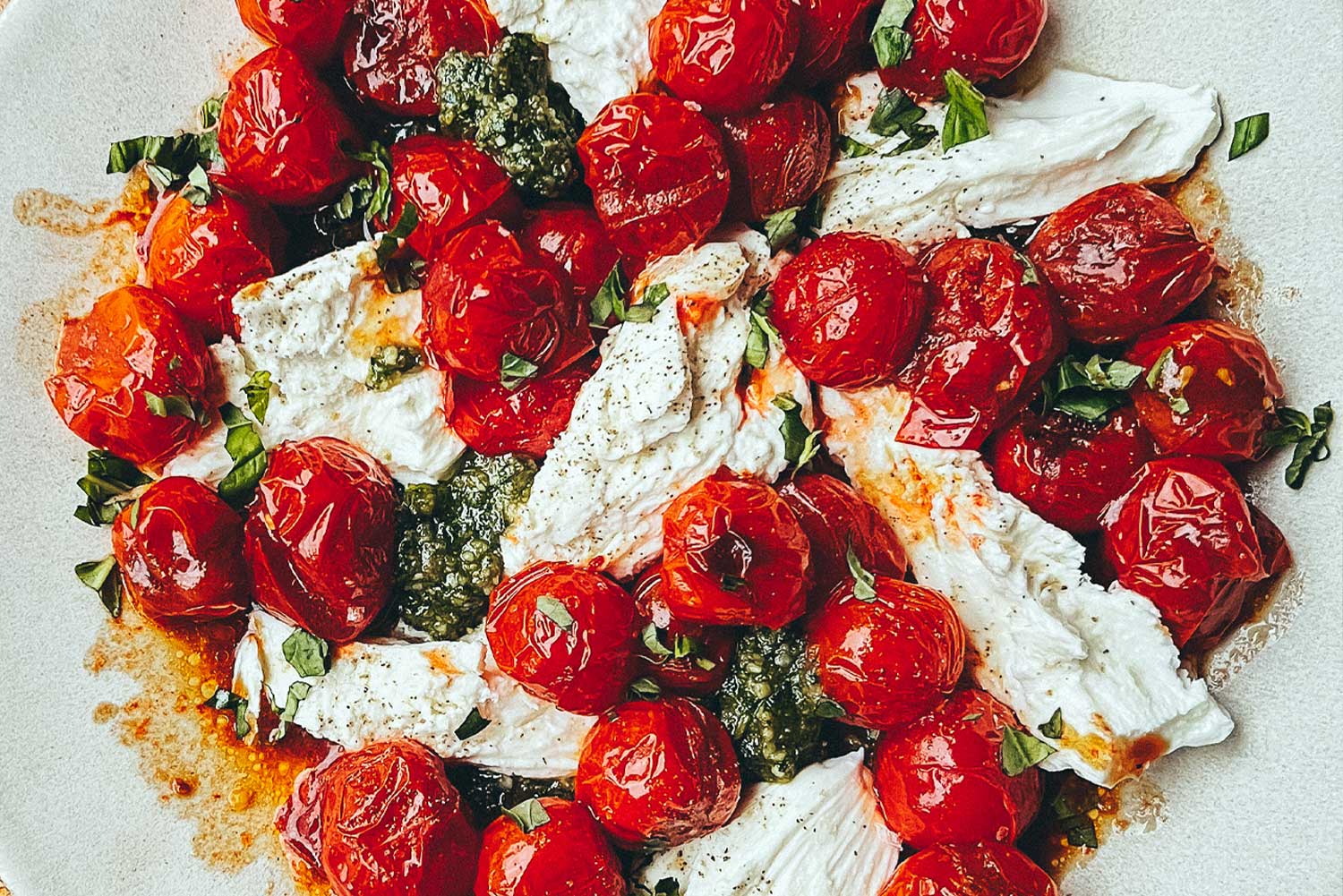 A plate of blistered cherry tomatoes, fresh mozzarella, and pesto sitting.