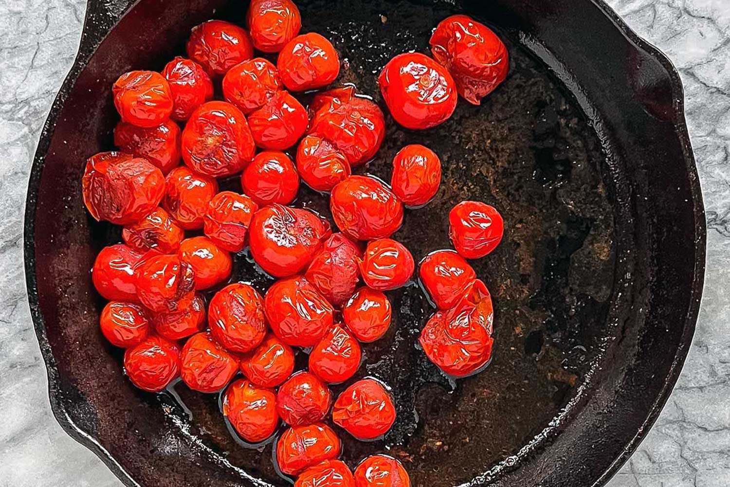 A cast iron pan filled with blistered red cherry tomatoes.