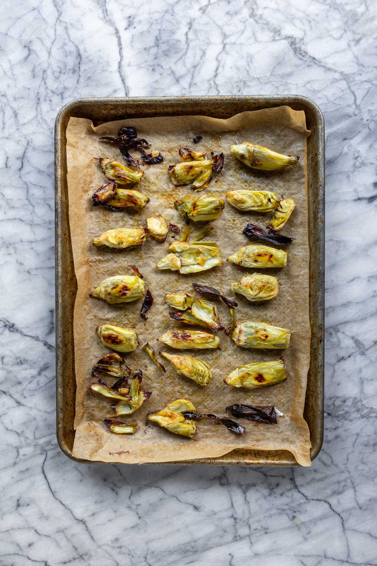 A baking sheet lined with parchment paper, with crispy baked artichoke hearts uniformly spaced on it.