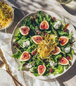 A large plate filled with a salad of figs, goat cheese, arugula, pecans, and frizzled leeks.