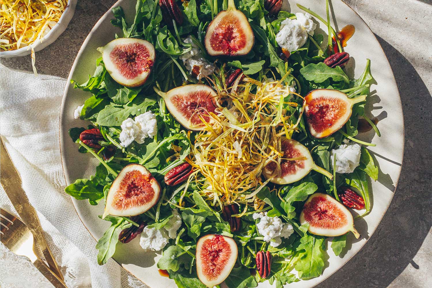 A plate filled with a fresh, late summer, fall seasonal salad of fresh figs, goat cheese, arugula, and toasted pecans, topped with a mound of frizzled leeks.