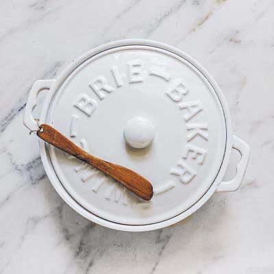 A white ceramic brie baker with a wooden serving spoon.