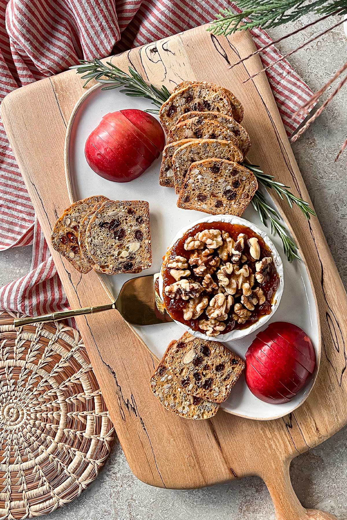 A top view of a table with a cheese board with a fresh Baked Brie And Preserves, paired with sliced apples, and crackers.