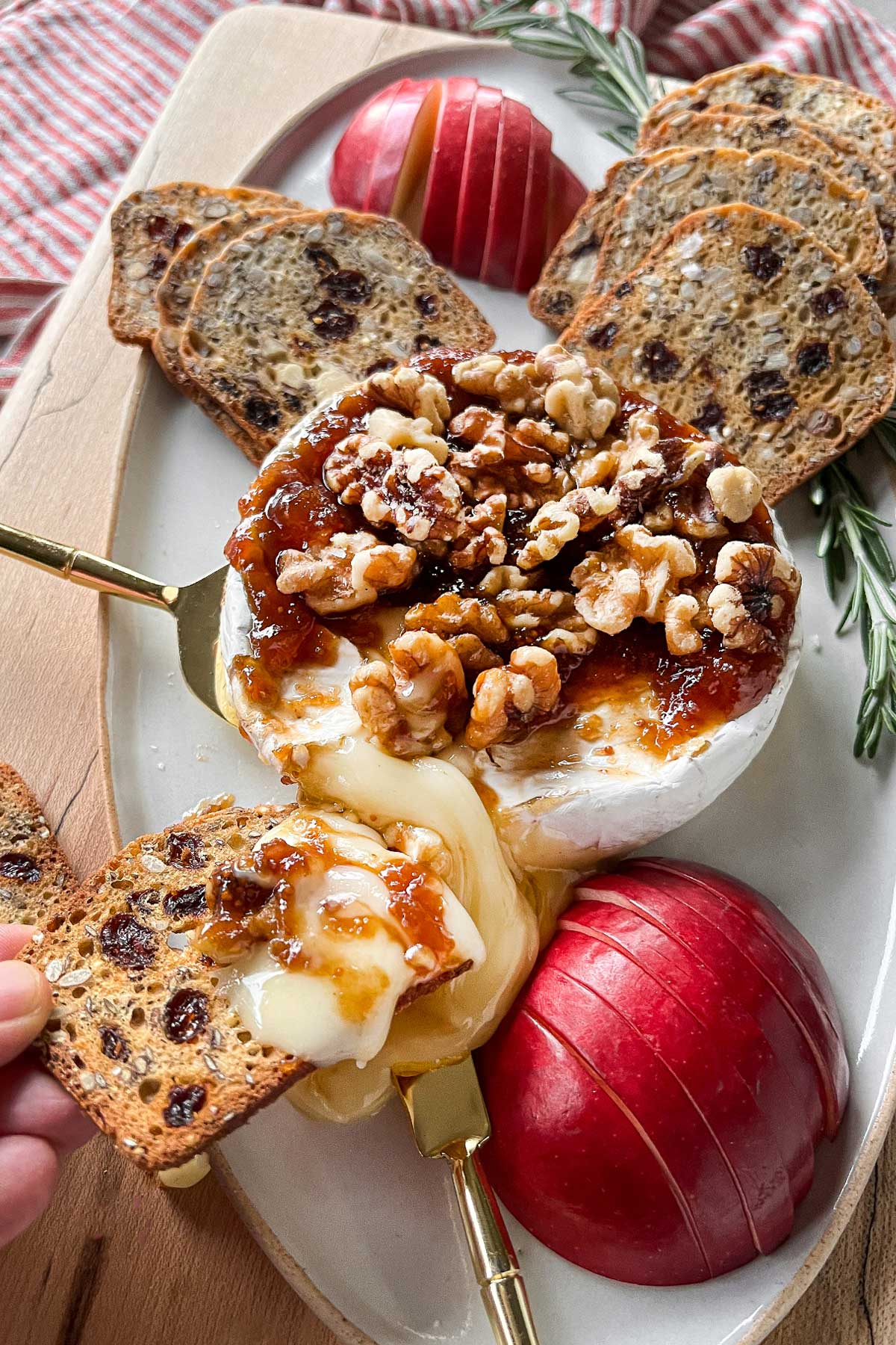 A close up of cheese board with a fresh Baked Brie And Preserves sliced open with melted brie pouring out.