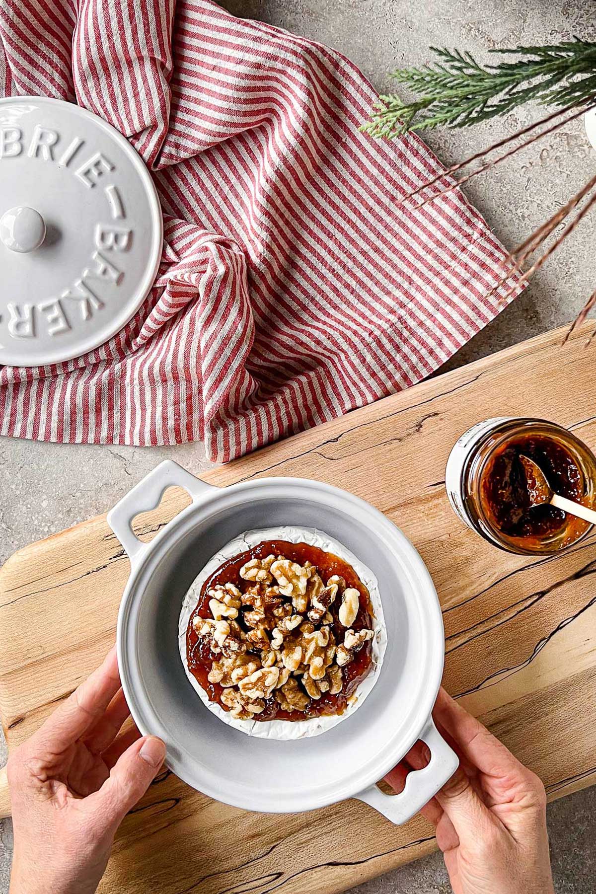 A brie spread with preserves and topped with walnuts, in a ceramic brie baker being prepped for the oven.