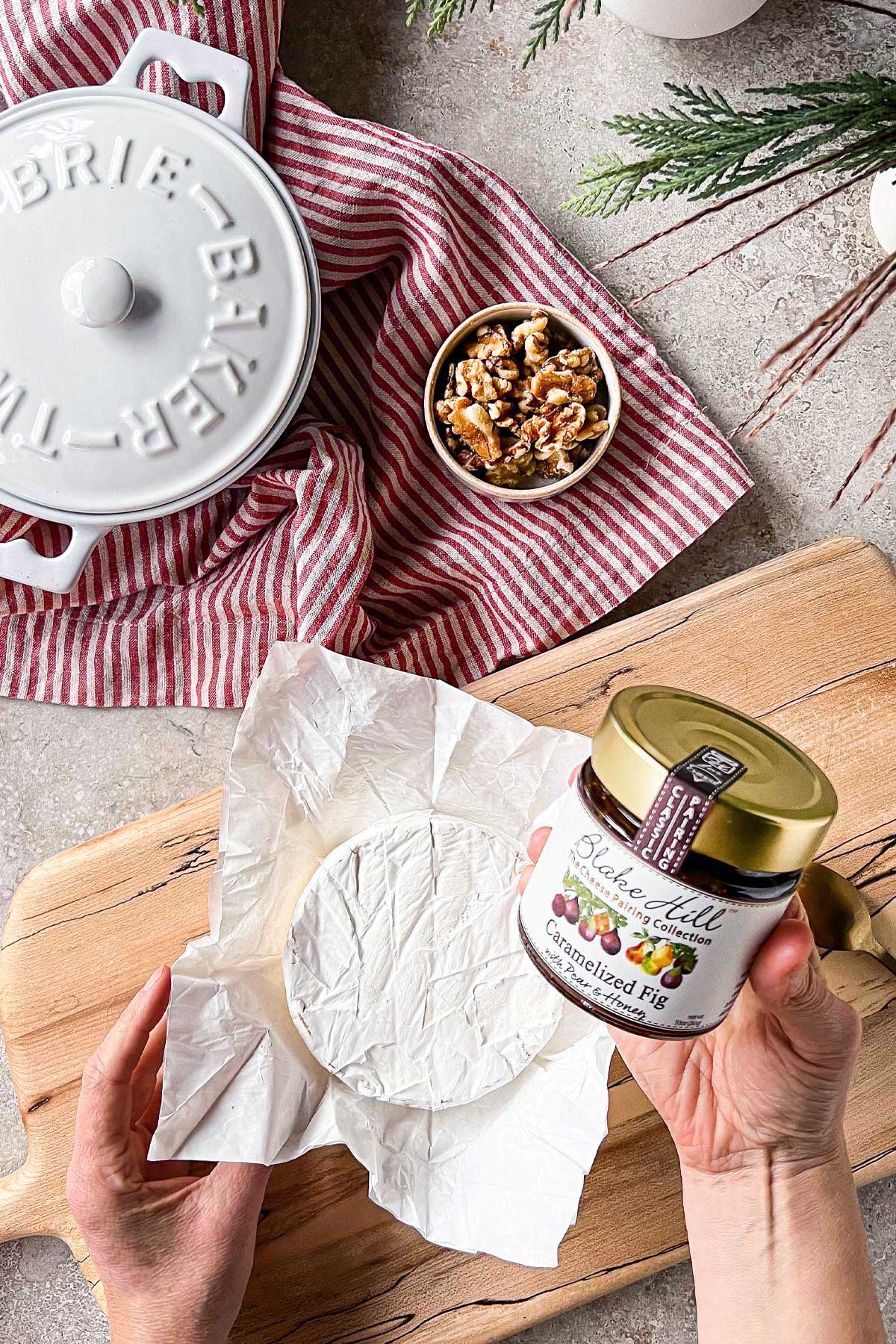 A brie cheese and a jar of Blake Hill Preserves Caramelized Fig Preserves with Pear & Honey being used in the preparation of a Baked Brie And Preserves recipe.