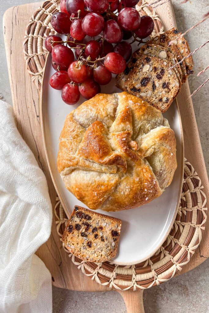 A ceramic platter on top of a maple serving board with a fresh from the oven Cranberry Baked Brie En Croûte. 