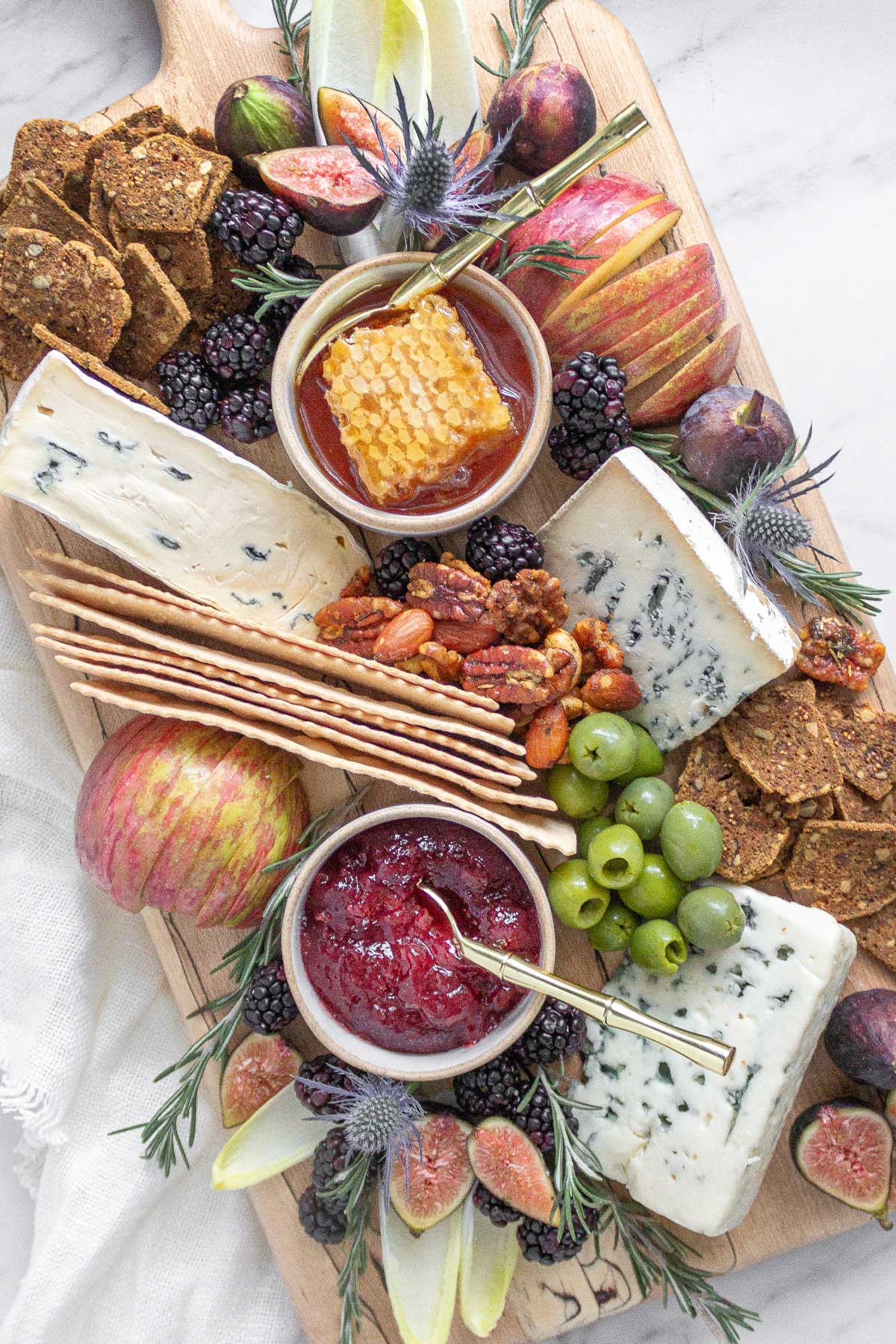 A cheese board with a selection of blue cheeses paired iwth apples, figs, blackberries, nuts, crackers, honeycomb, and fruit jam.