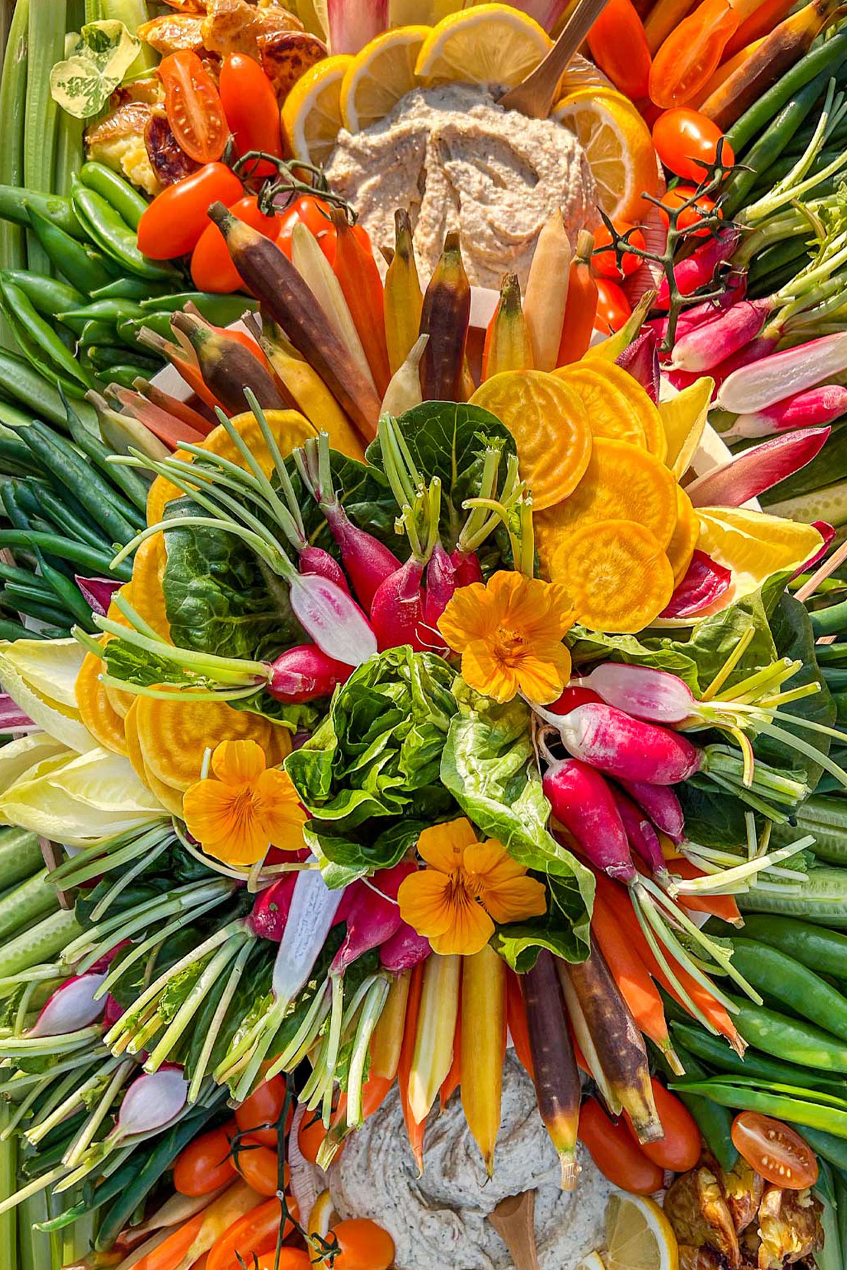 A large fresh vegetable crudité platter filled with fresh vegetables, lettuces, herbs, and flowers.