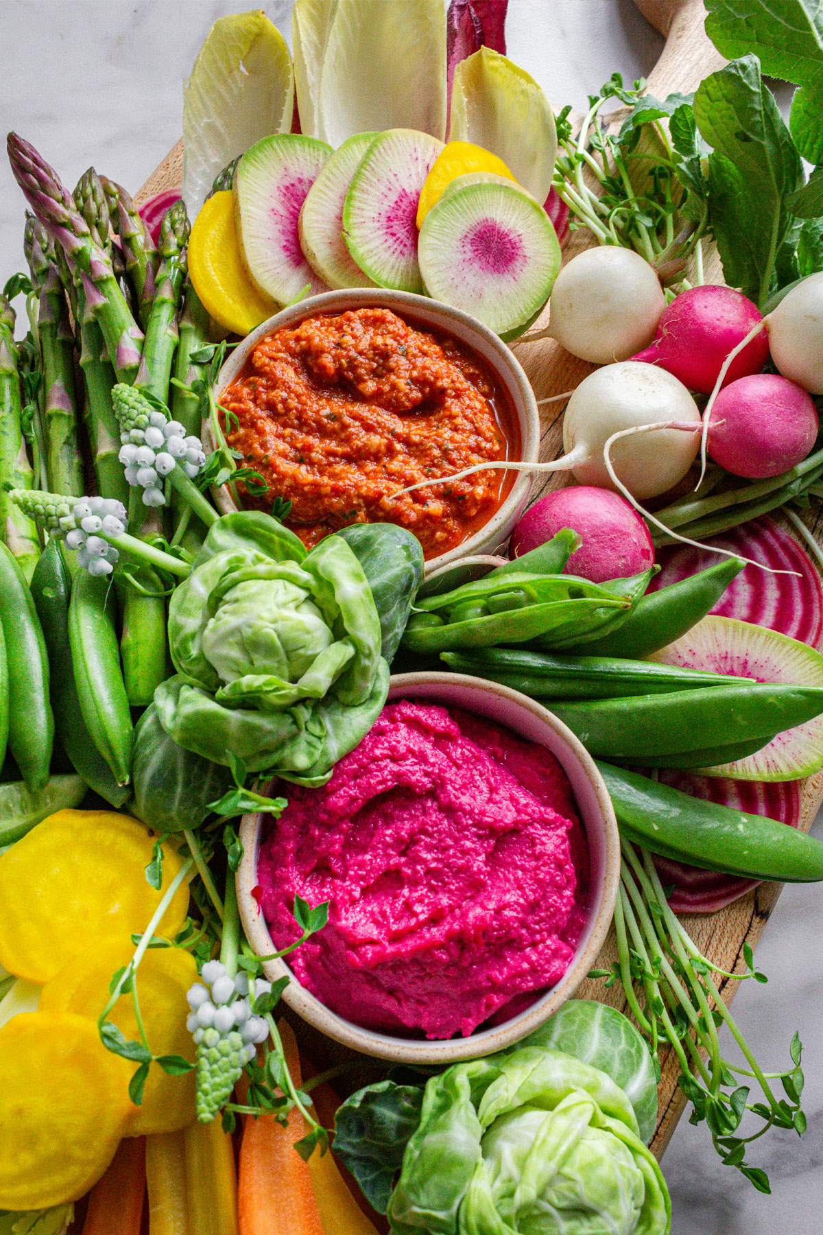 A spring crudité platter filled with spring vegetables like peas, radishes, golden beets, and carrots.