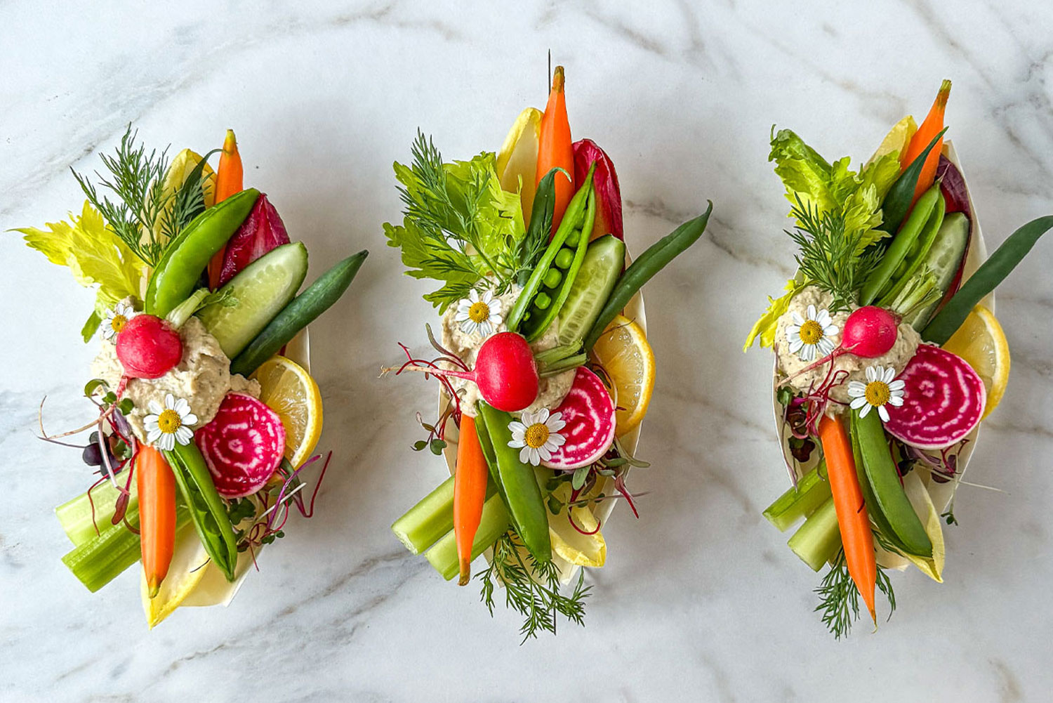 A trio of handheld crudité boat appetizers in palm leaf bowls.