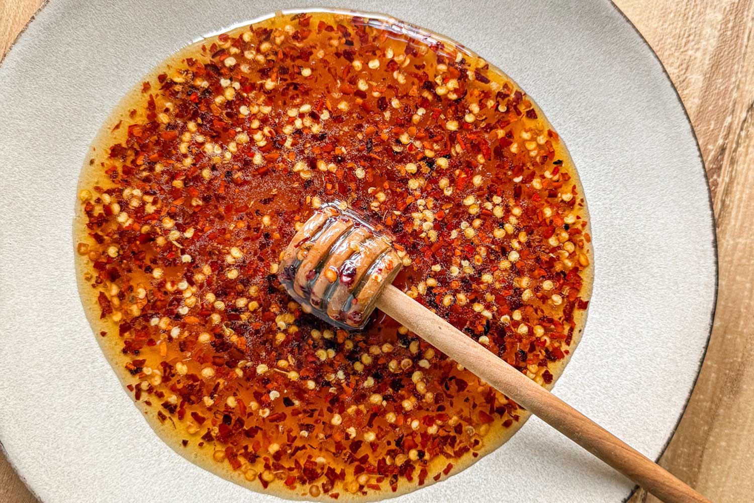 Hot honey infused with red chili peppers in a bowl on a wooden serving board, with a honey dipper in it.