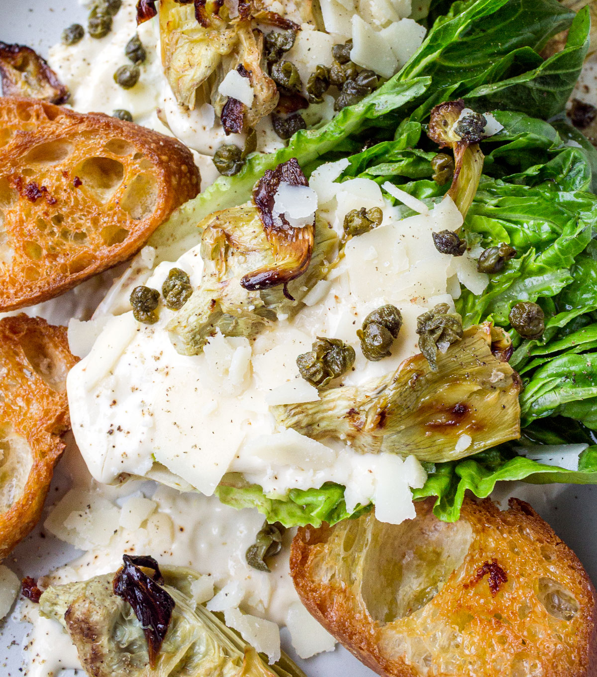Romaine lettuce wedges drizzled with a creamy Caesar dressing and topped with baguette croutons and capers.