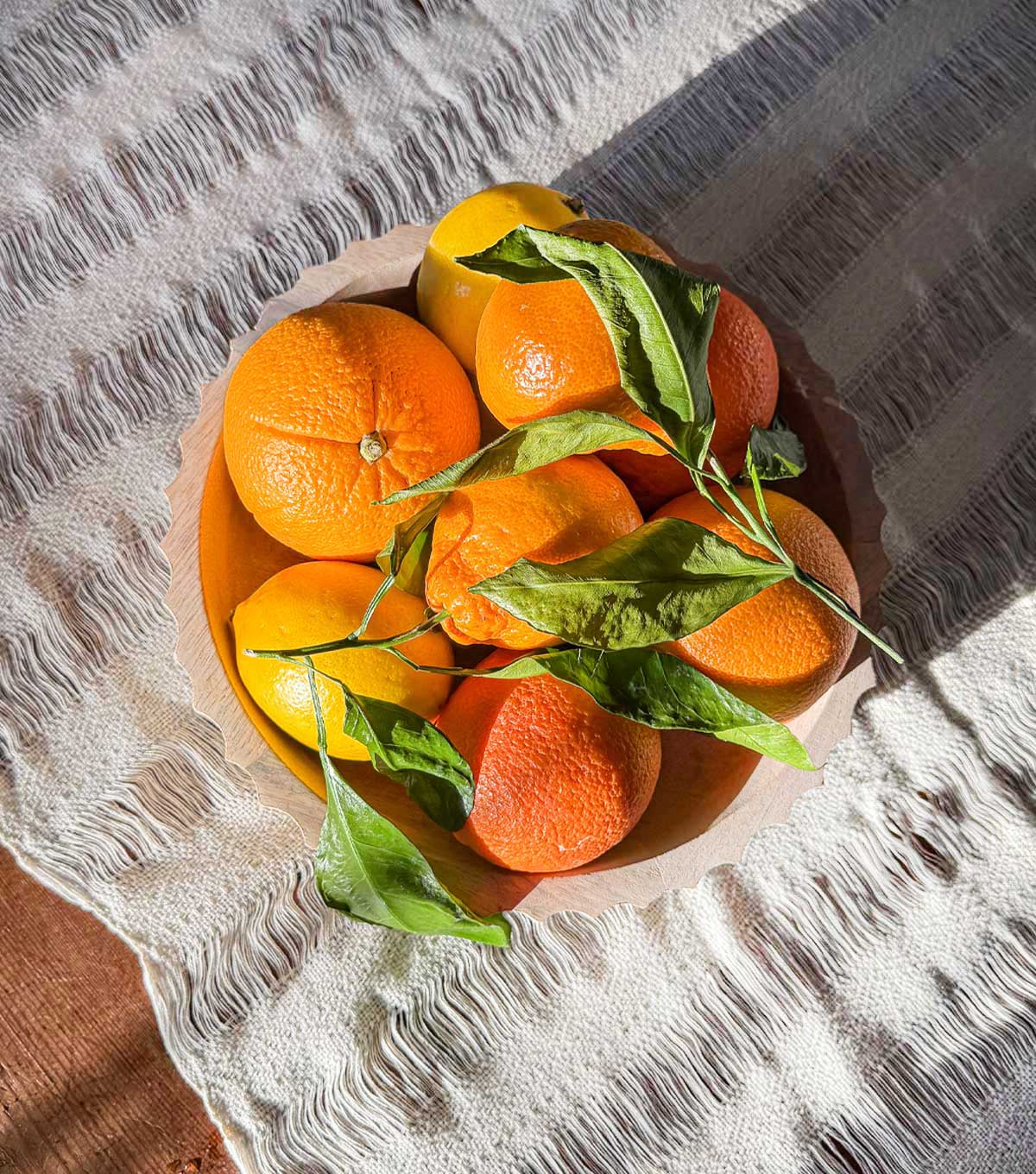 A bowl of citrus fruits in the bright winter light, sitting on a hand loomed ivory runner.