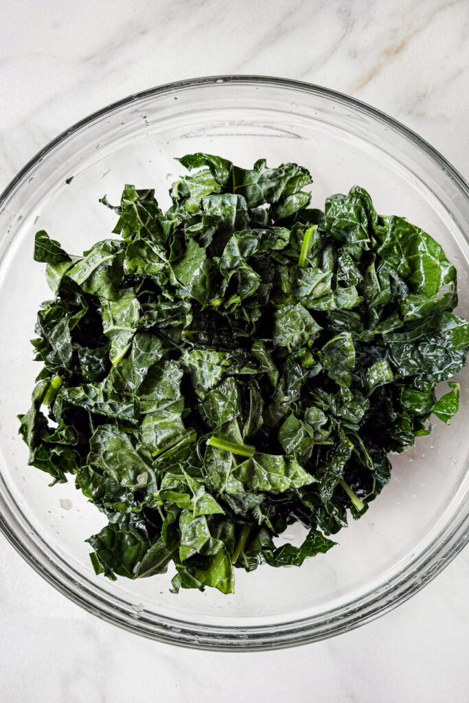 A bowl of massaged lacinato kale, sitting on a marble countertop.