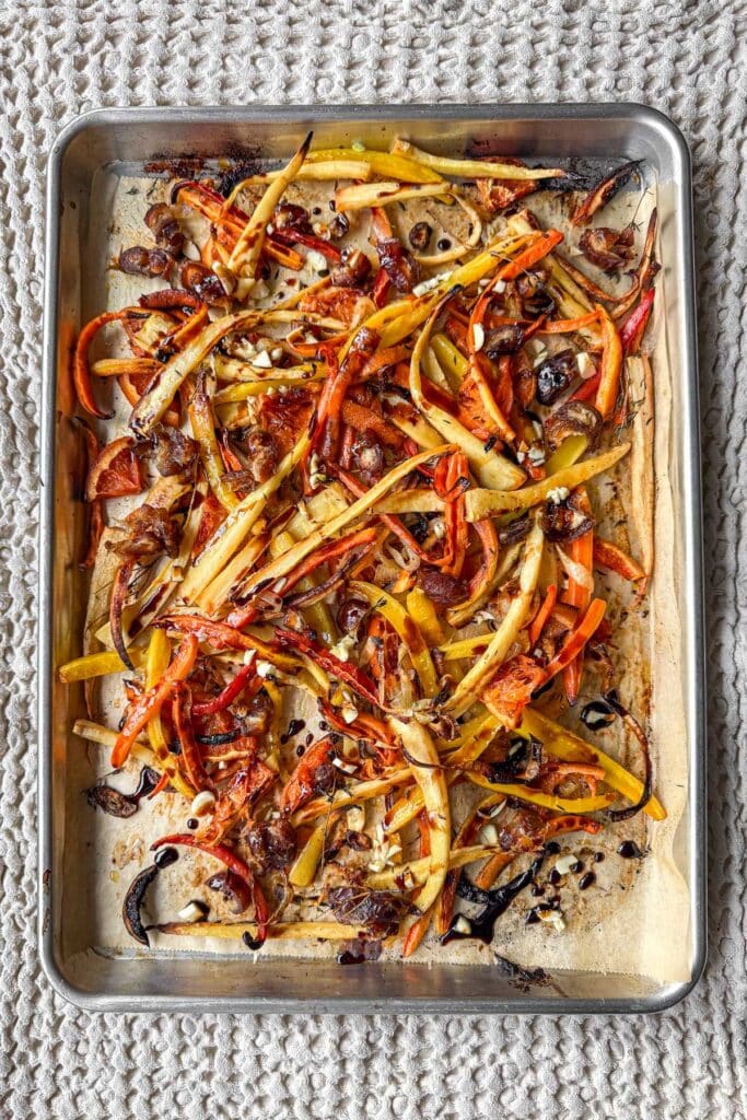 A sheet pan filled with roasted and caramelized finely cut parsnips, rainbow carrots, Cara Cara oranges, onions, and thyme.