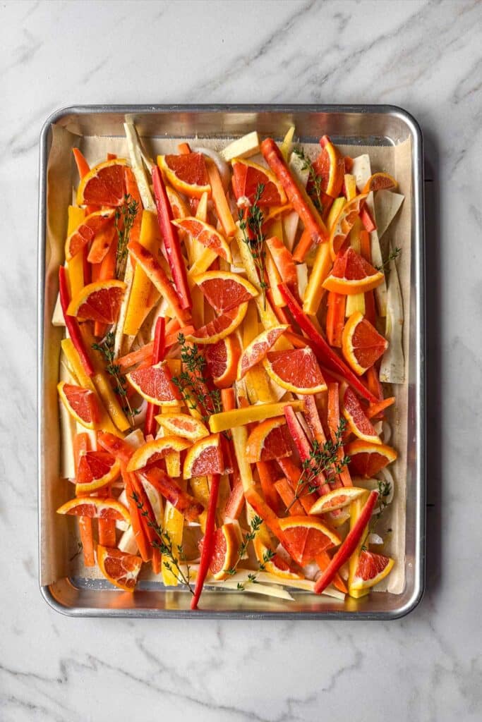 A sheet pan filled with finely cut parsnips, rainbow carrots, Cara Cara oranges, onions, and thyme.