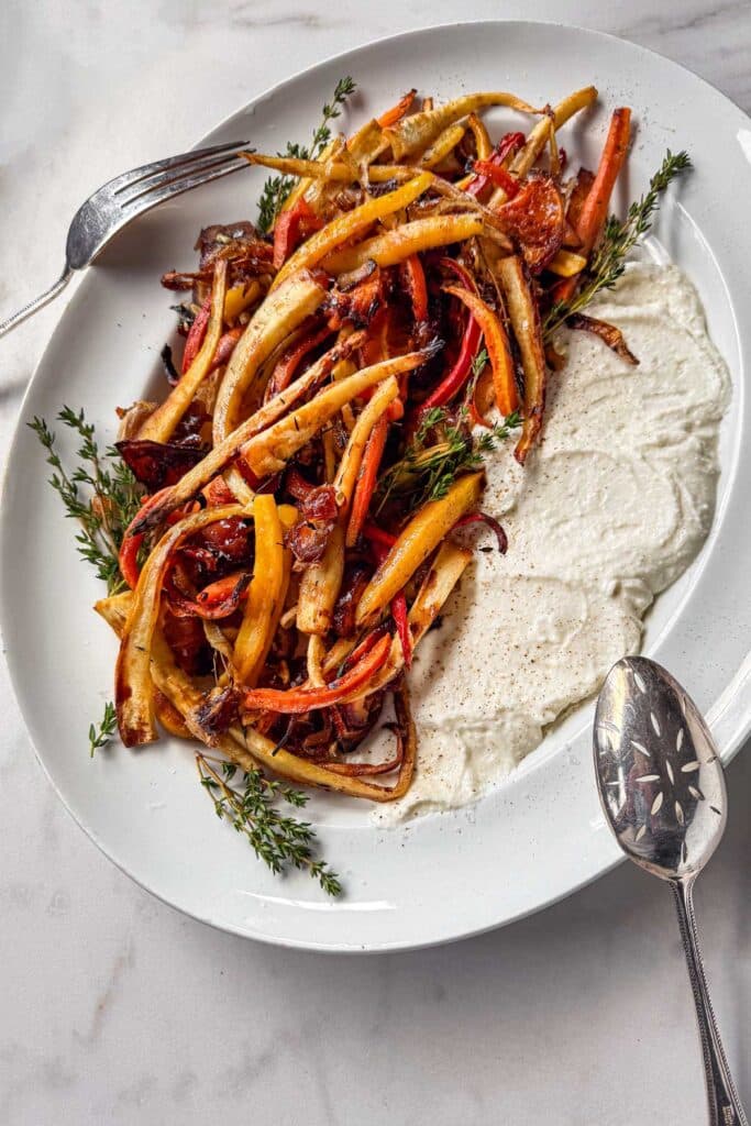 A serving platter with a generous smear of whipped feta finished with caramelized parsnips, carrots, and oranges with sprigs of fresh thyme tucked in.