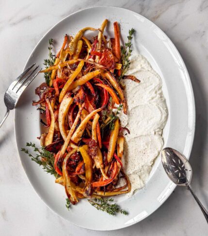 An oval serving platter with roasted caramelized parsnips, carrots, thyme, with a generous smear of whipped feta.