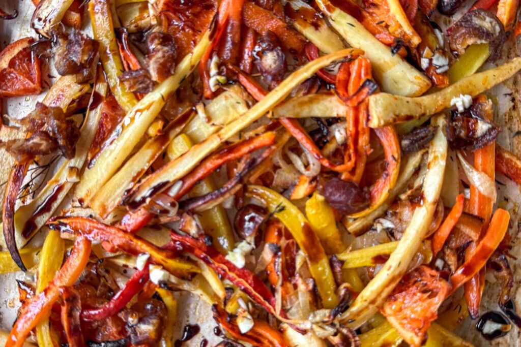 A close up of a sheet pan filled with roasted and caramelized finely cut parsnips, rainbow carrots, Cara Cara oranges, onions, and thyme.