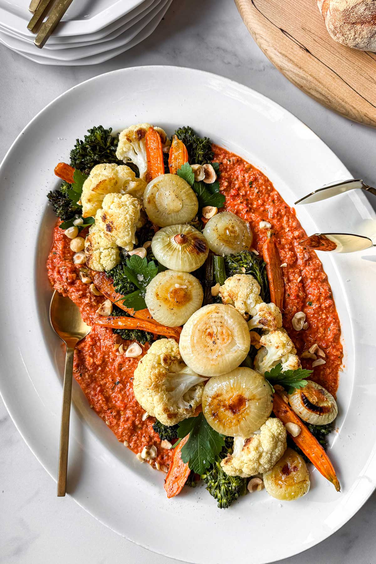 A serving platter of romesco sauce is layered with warm roasted winter vegetables: cippolini onions, broccolini, carrots, and cauliflower.