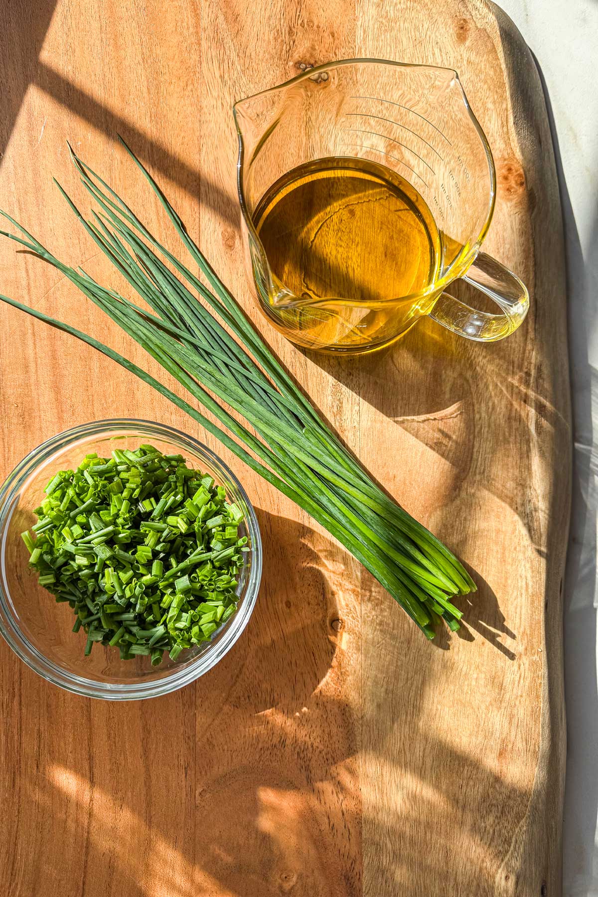 The ingredients for fresh chive oil, placed on a wooden board: fresh chives and extra virgin olive oil.