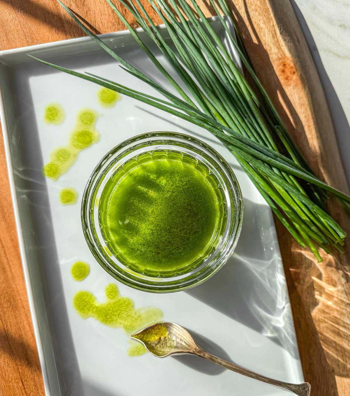 Bright green chive oil in a glass jar with fresh chives on a tray and drizzled oil on a plate