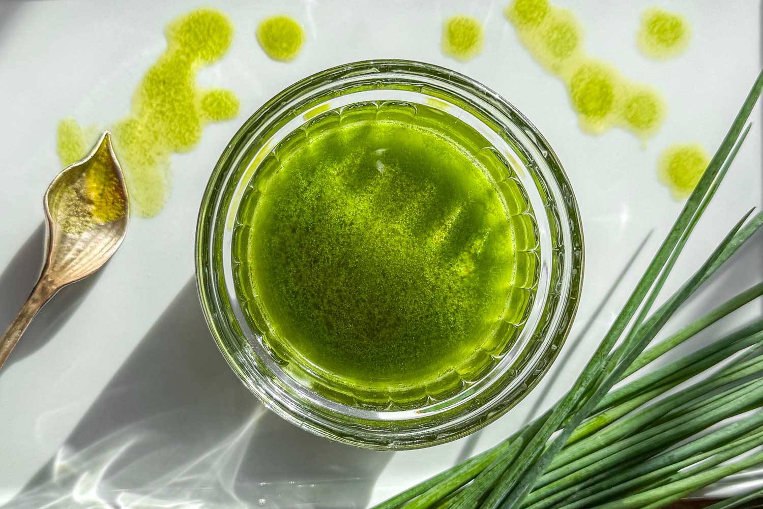 Bright green chive oil in a glass jar with fresh chives on a tray and drizzled oil on a plate