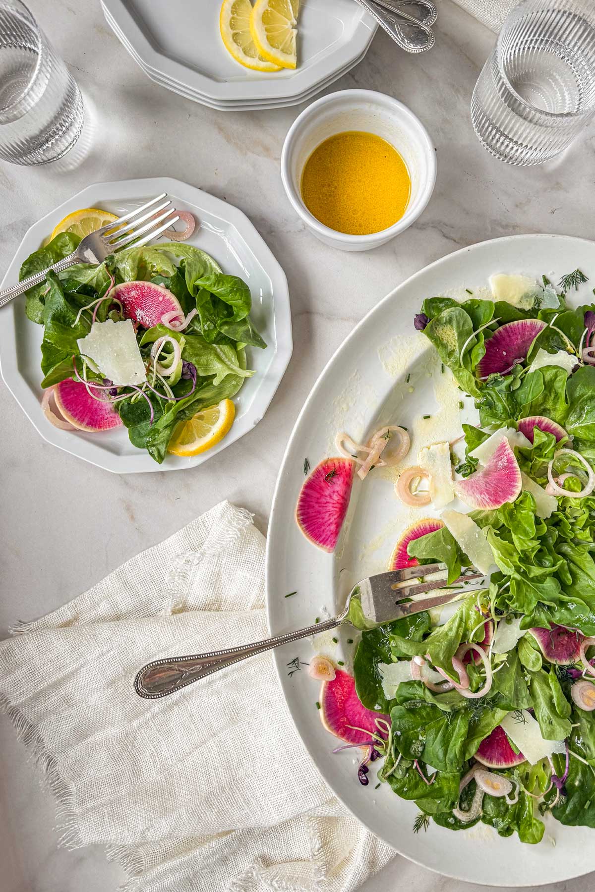 Early spring greens salad with butter lettuce, watermelon radishes, shaved parmesan, and pickled shallots on a white plate